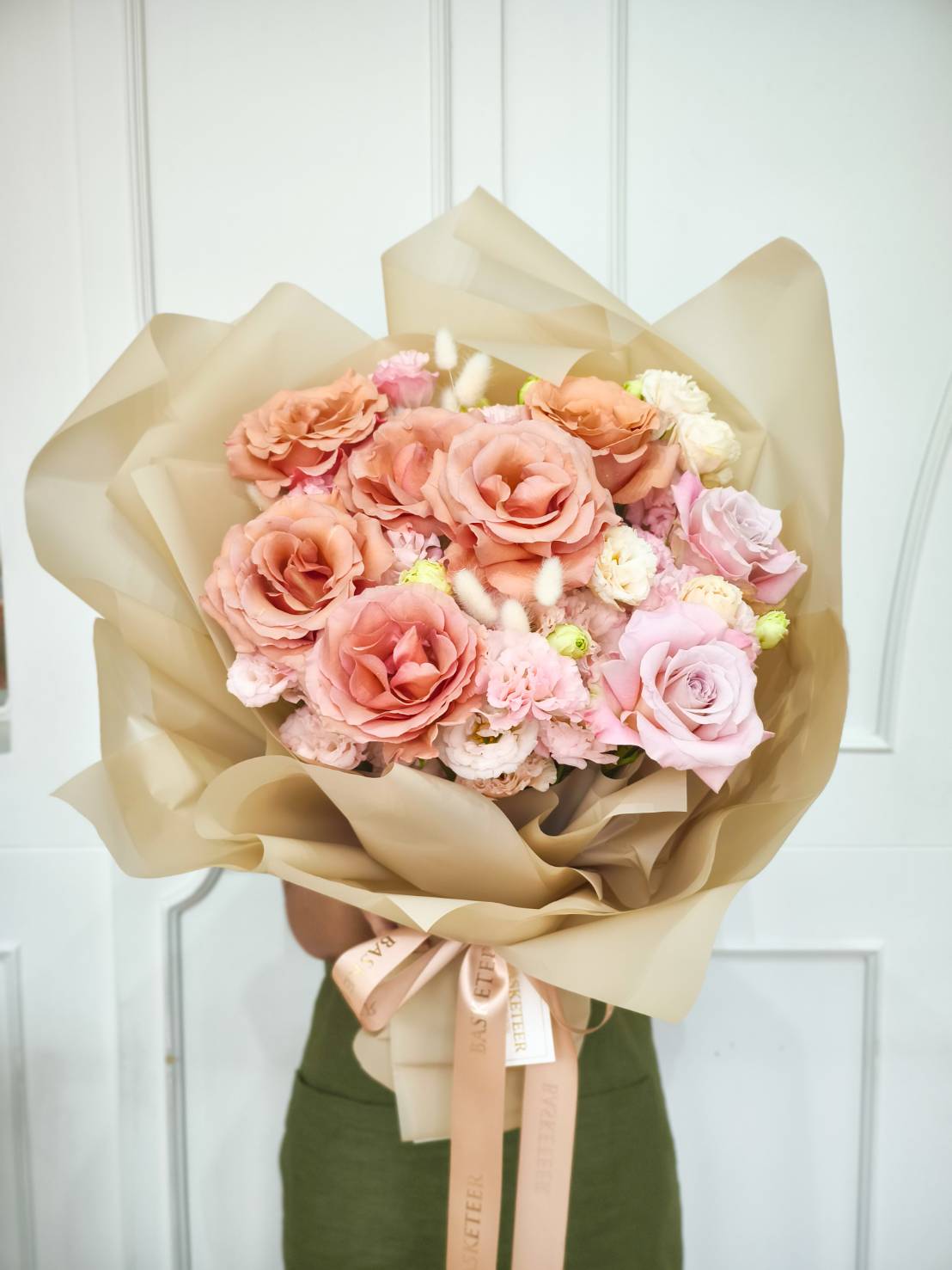 Elegant bouquet of peach and pink roses with pastel blooms, wrapped in champagne gold paper and tied with satin ribbons.