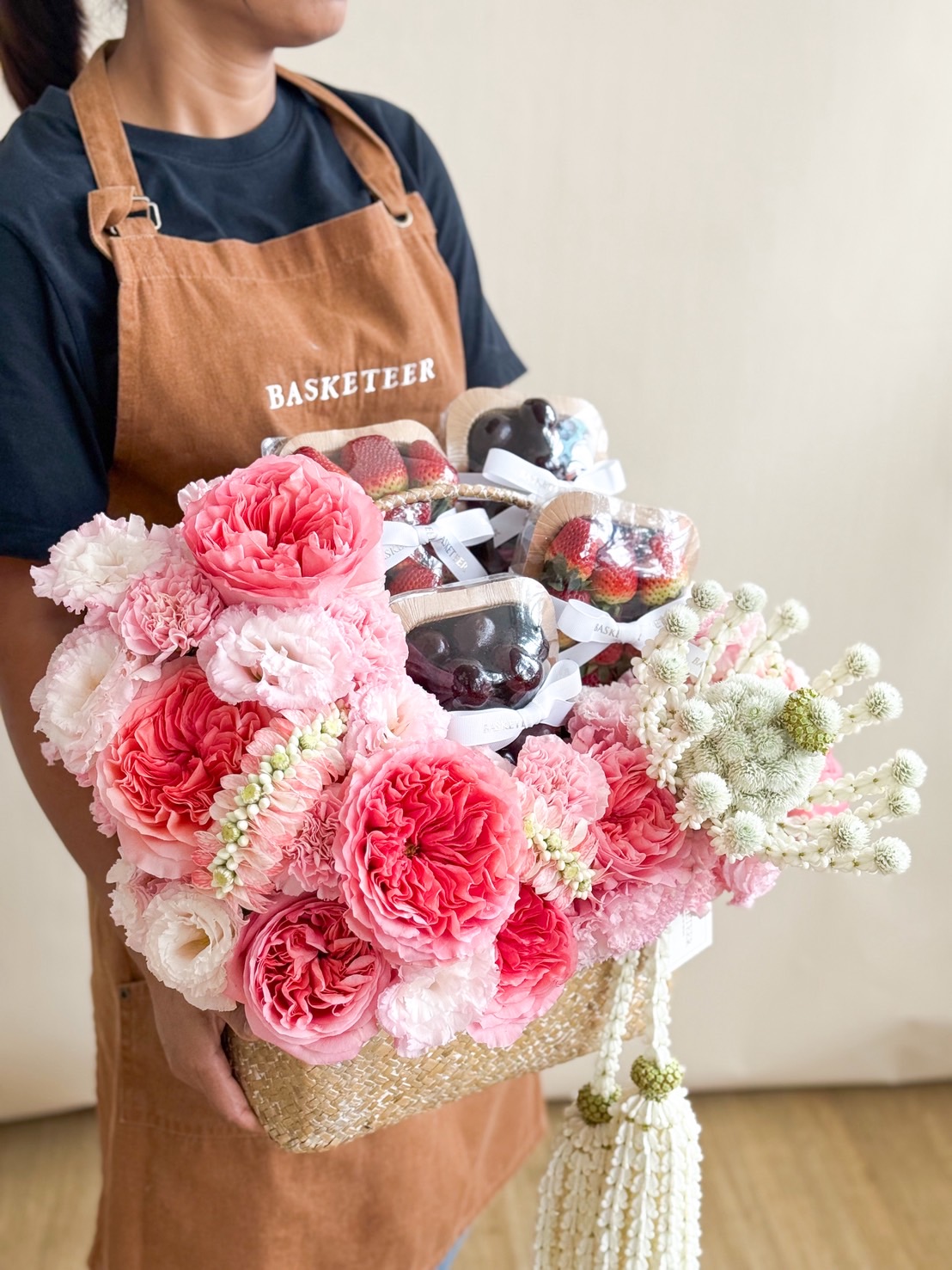 Staff holding a luxury woven basket with pink roses, carnations, and peonies, fresh fruits, and a traditional Thai jasmine garland.