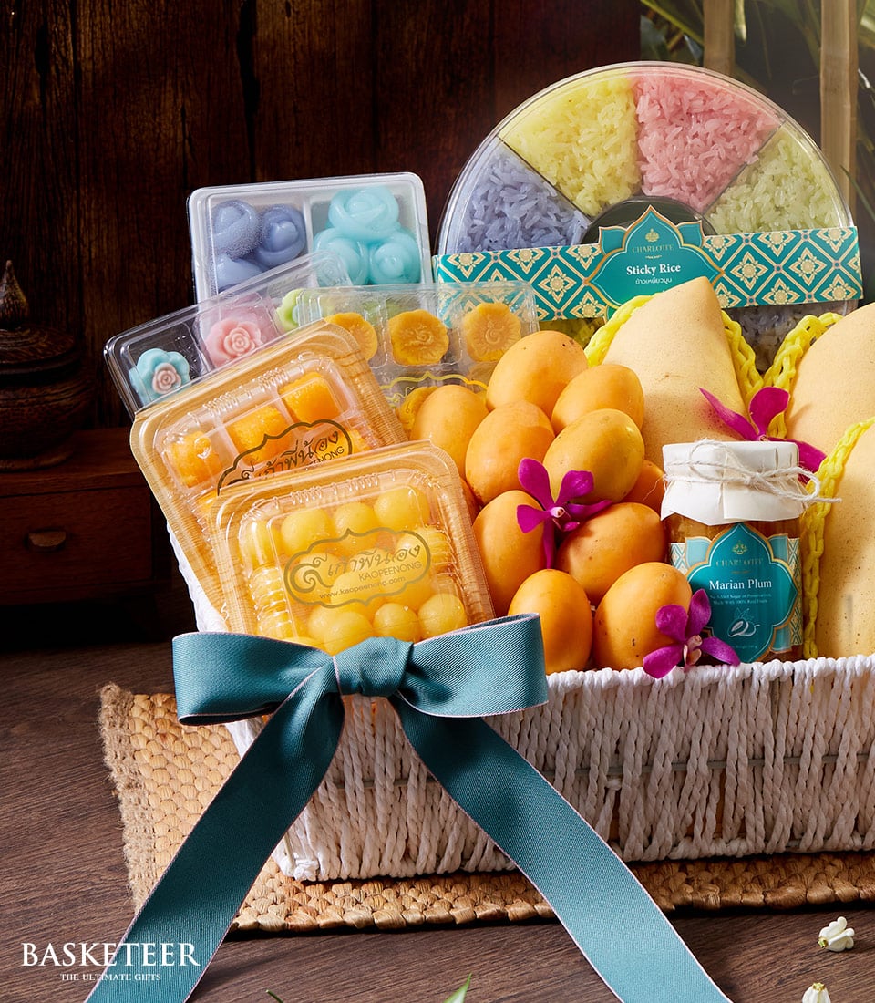 A luxurious Thai Tropical Desserts Basket elegantly curated by Basketeer, featuring an array of exquisite delights. Nestled within are vibrant yellow traditional Thai desserts in sleek plastic containers, multi-hued sections of decadent sticky rice, and succulent fresh Marian plums. The entire presentation is artfully accented with a festively tied teal ribbon bearing the distinguished Basketeer logo, creating an inviting and opulent visual feast.