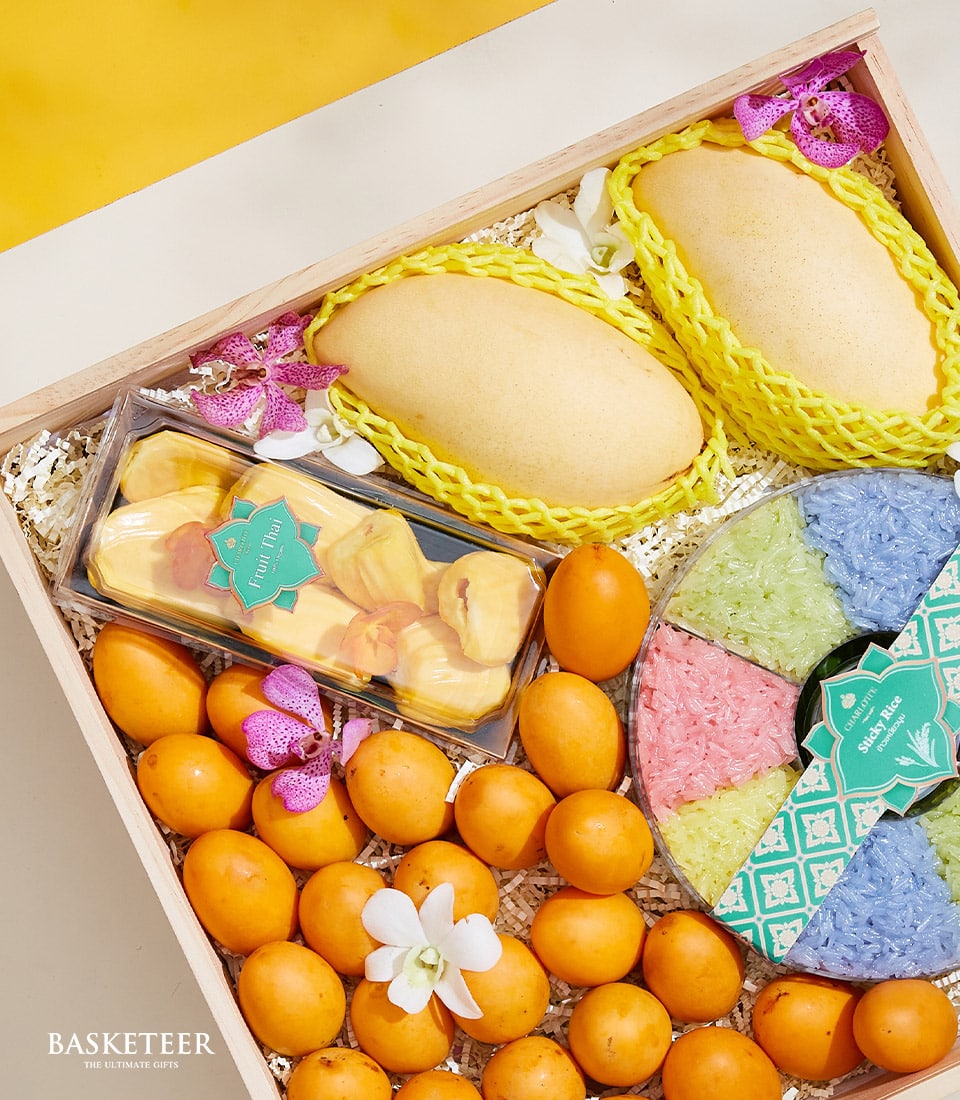 Indulge in the exquisite Thai Fruits Sticky Rice Set, presented in a luxurious wooden gift box adorned with The Basketeer branding. This lavish set features two golden-hued mangoes, a delectable package of sliced jackfruit, and a vibrant cluster of petite orange fruits. At its heart is an artful arrangement of multicolored sticky rice portions, elegantly arrayed in hues of green, white, yellow, and blue. Ideal for gifting or savoring yourself, this set bursts with opulence and inviting flavors that are synonymous with The Basketeer experience.