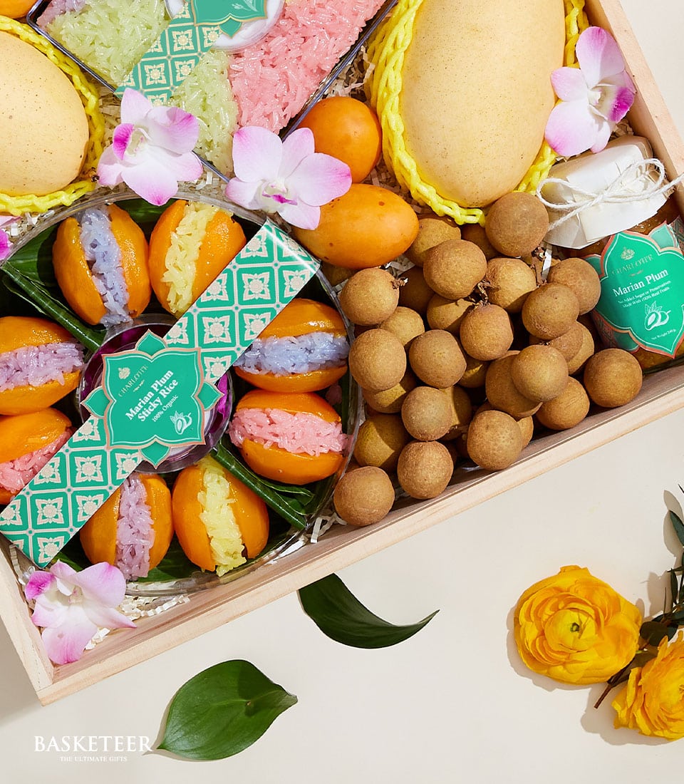 A beautifully crafted wooden tray showcases an array of mango sticky rice desserts in vibrant, colorfully designed packaging adorned with elegant green and white patterned labels reading 
