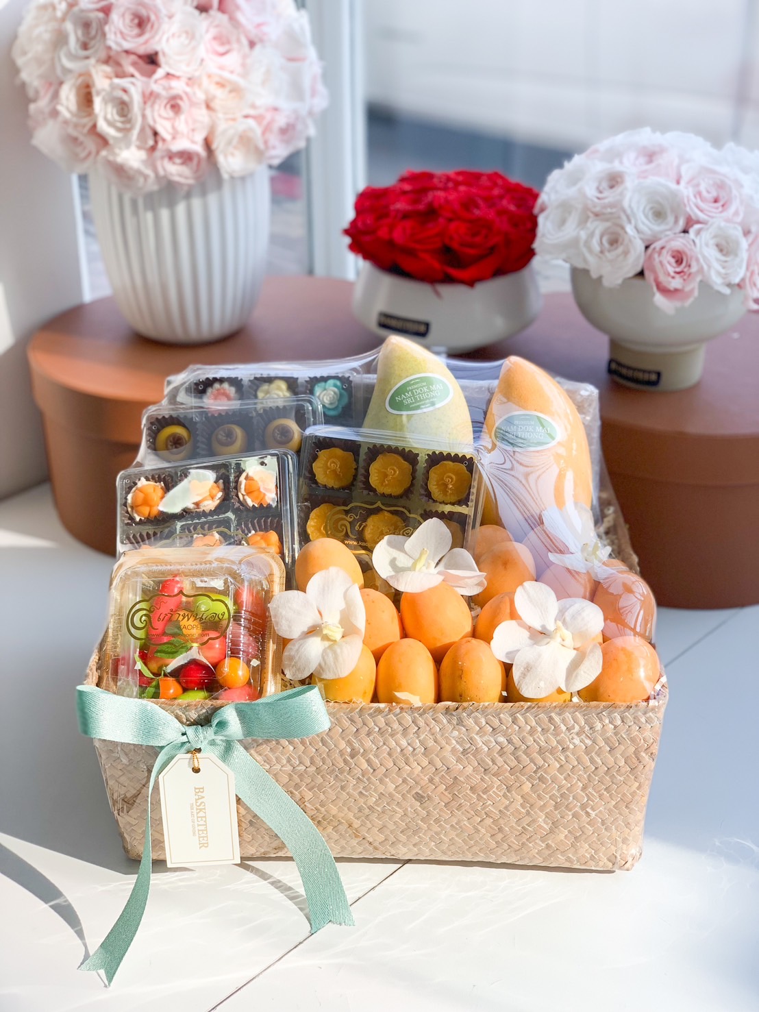 Woven gift basket with Nam Dok Mai mangoes, Mayongchid fruits, Thai desserts, and white orchids