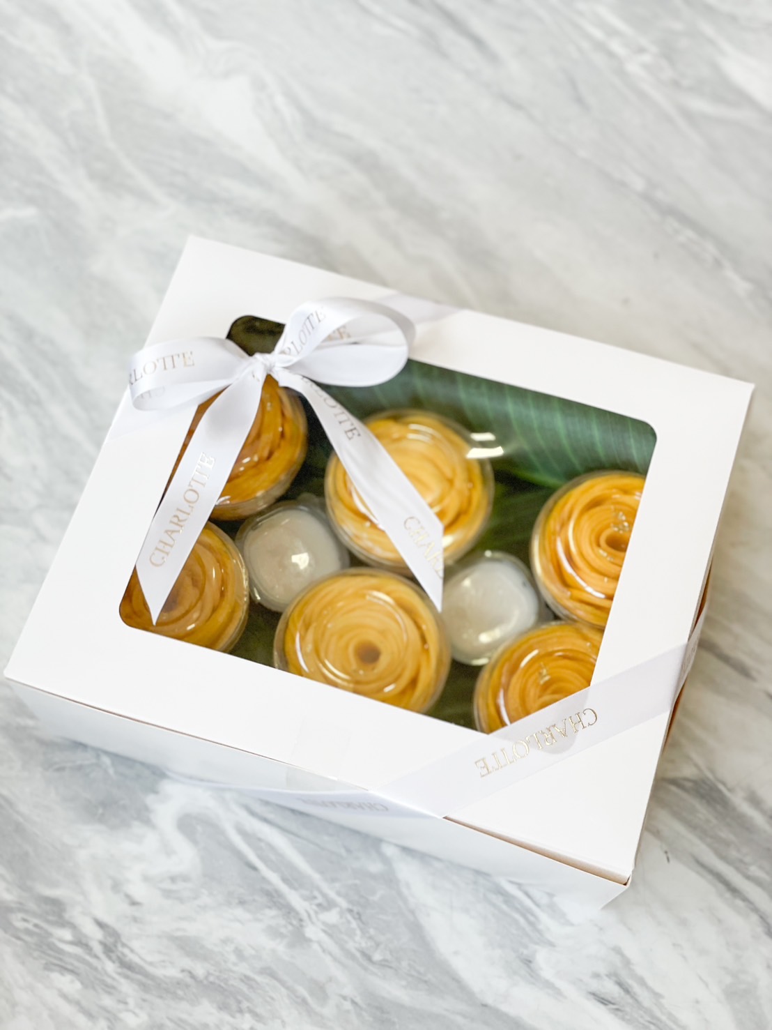 A beautifully packaged Thai dessert gift box featuring golden Thai custard (Sangkaya) and coconut pudding, elegantly tied with a white ribbon.