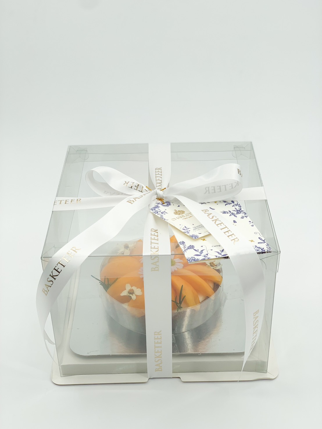 Mini marian plum tart in a transparent gift box with white ribbon and floral tag.