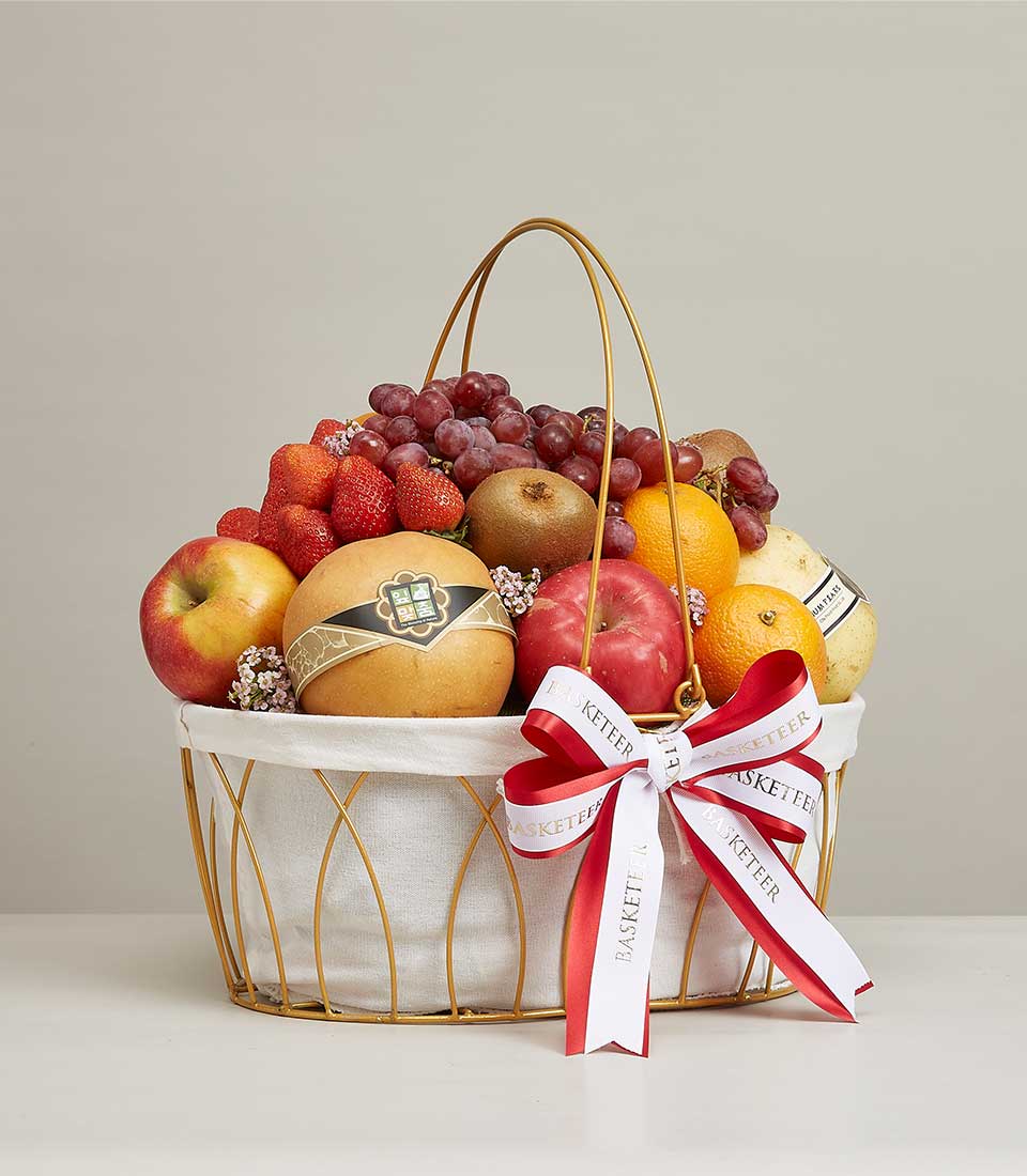 Large gold-colored steel frame gift basket Contains a variety of fresh fruits such as red grapes, green kiwis, oranges, and many more. Decorated with ribbon bows. Red and white with the word 