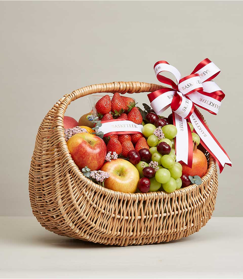 Brown Rattan Gift Basket Filled with a variety of fresh fruits such as red strawberries, red pomegranates, red cherries, and many more. It is decorated with a red and white ribbon bow with 