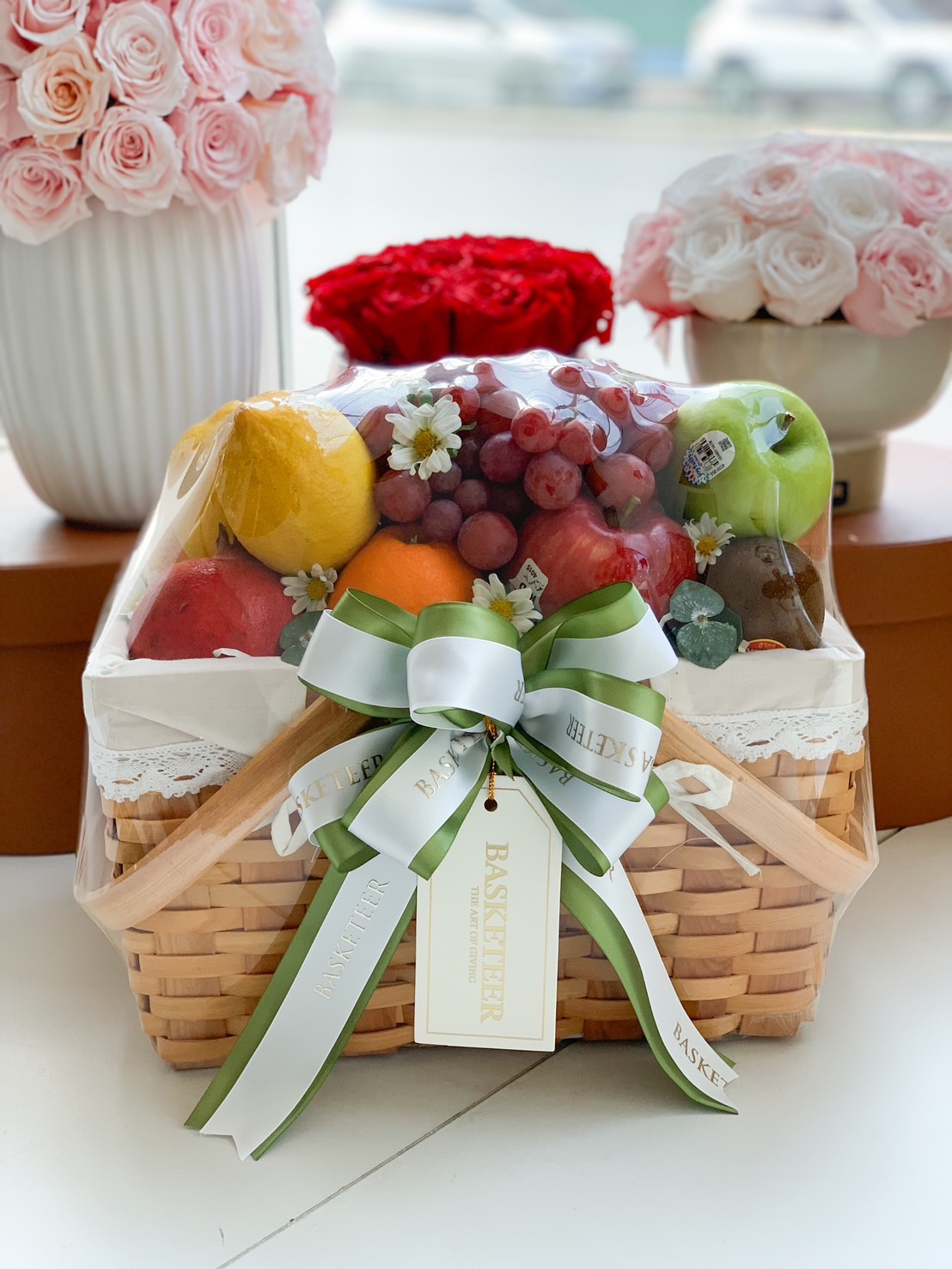 A gourmet fresh fruit gift basket featuring premium apples, grapes, pears, citrus, and kiwi, elegantly arranged in a handwoven basket with lace detailing and a decorative green ribbon. A perfect choice for health-conscious gifting, celebrations, and corporate events.
