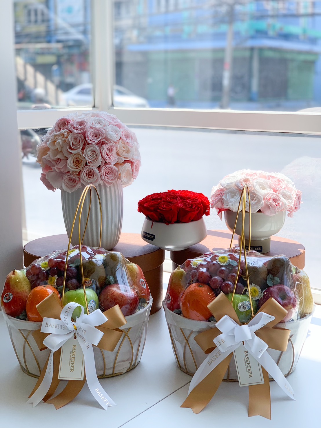 A beautifully arranged fresh fruit gift basket, featuring premium apples, pears, oranges, grapes, and exotic fruits, elegantly wrapped with a gold and white satin ribbon and a Basketeer gift tag. Perfect for corporate gifts, celebrations, and get-well wishes.