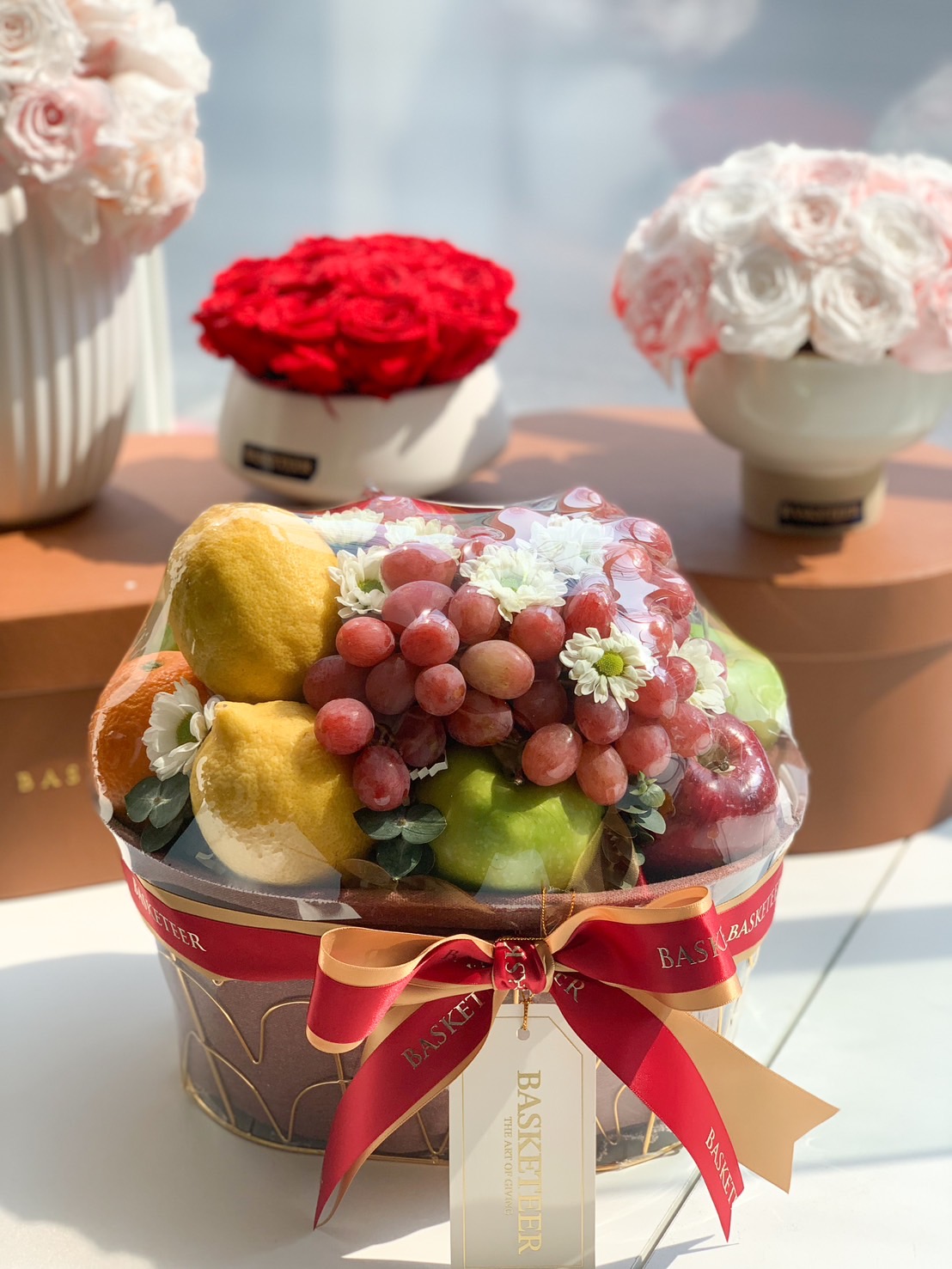 Premium fruit gift basket with red grapes, apples, and assorted fruits wrapped in clear cover and decorated with red ribbon.