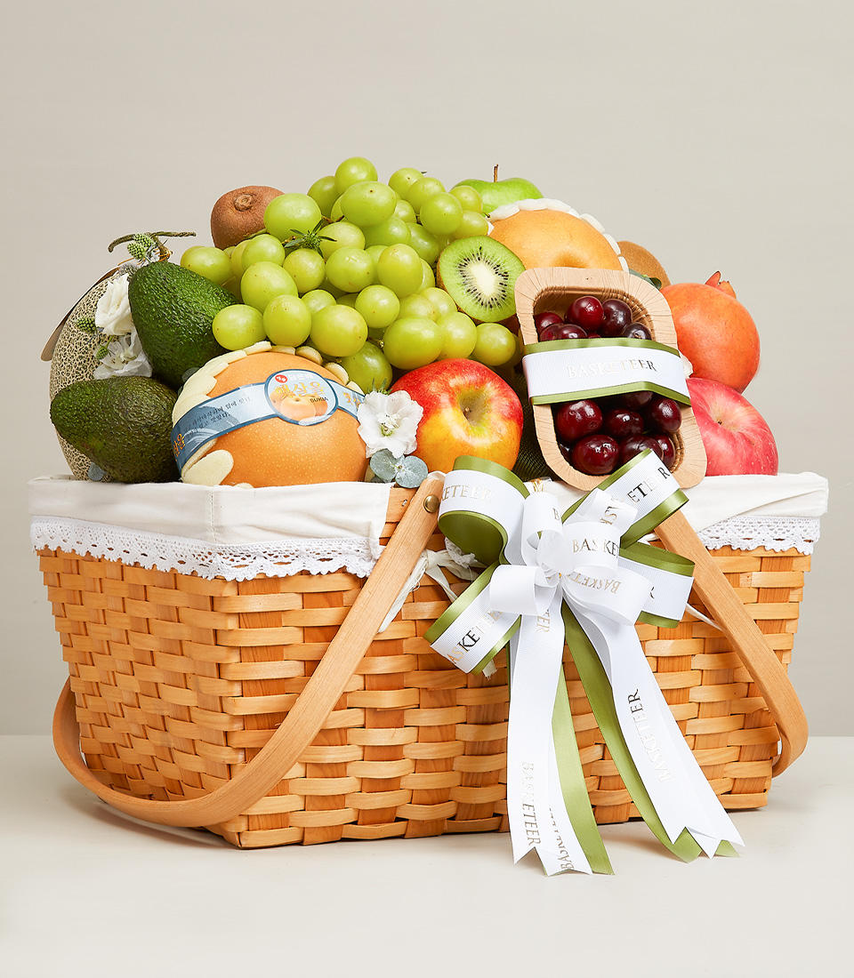 Brown rattan gift basket with fabric lining inside. It is filled with a variety of fresh fruits such as green grapes, red apples, and yellow Chinese pears. and many others Decorated with a green and white ribbon bow with 