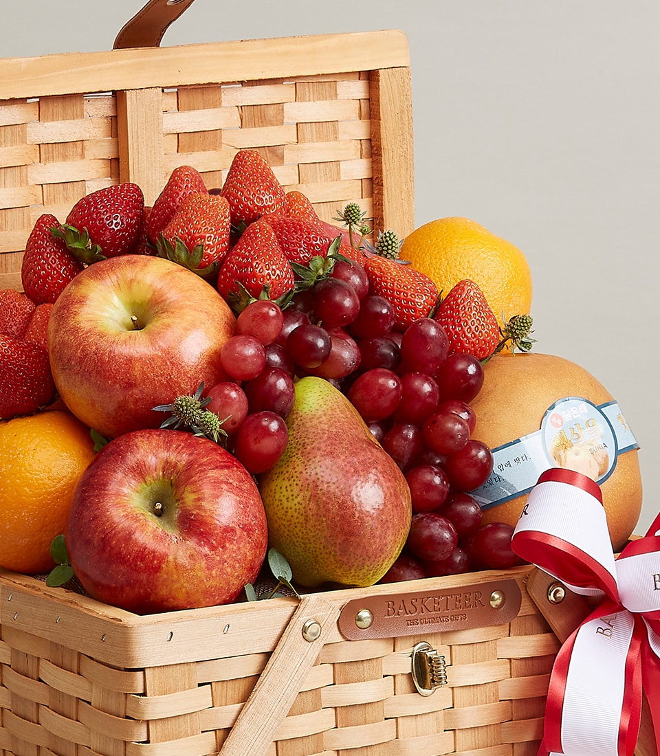 Introducing the Basketeer Sumptuous Fruit Bliss Basket, an indulgent showcase of nature's finest bounty. Nestled in an elegantly woven wicker basket, this luxurious assortment features crisp apples, vibrant oranges, succulent strawberries, luscious grapes, and a perfectly ripened pear. Adorned with a sophisticated red and white ribbon bearing the distinguished Basketeer logo, each piece of fruit is thoughtfully wrapped in protective foam to ensure pristine condition. This inviting presentation promises both visual appeal and fresh delight for any discerning recipient.