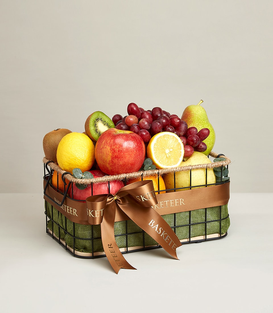 A luxurious wire basket overflowing with an exquisite selection of premium fruits, featuring a crisp apple, zesty lemon, luscious pear, succulent grapes, vibrant kiwi, and a perfectly sliced orange. The Gourmet Fruit Gift Basket is elegantly tied with a rich brown ribbon emblazoned with the prestigious 