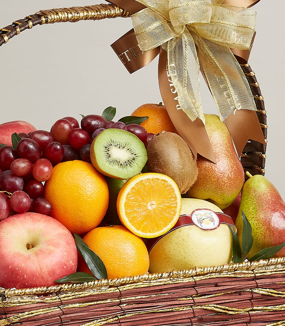A lavish mixed fruit basket filled with a colorful assortment of fruits, including apples, oranges, pears, grapes, and kiwis. A gold and brown ribbon is tied to the basket's handle, adding an elegant touch. An orange slice is prominently displayed in front.
