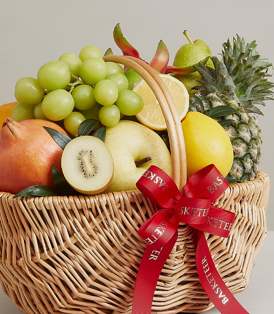 A luxurious Gala Fruit Extravaganza Basket overflowing with a bountiful selection of fresh grapes, crisp apples, a regal pineapple, luscious pomegranate, and vibrant kiwi. This exquisite wicker basket is elegantly accented with a rich red ribbon showcasing the distinguished 