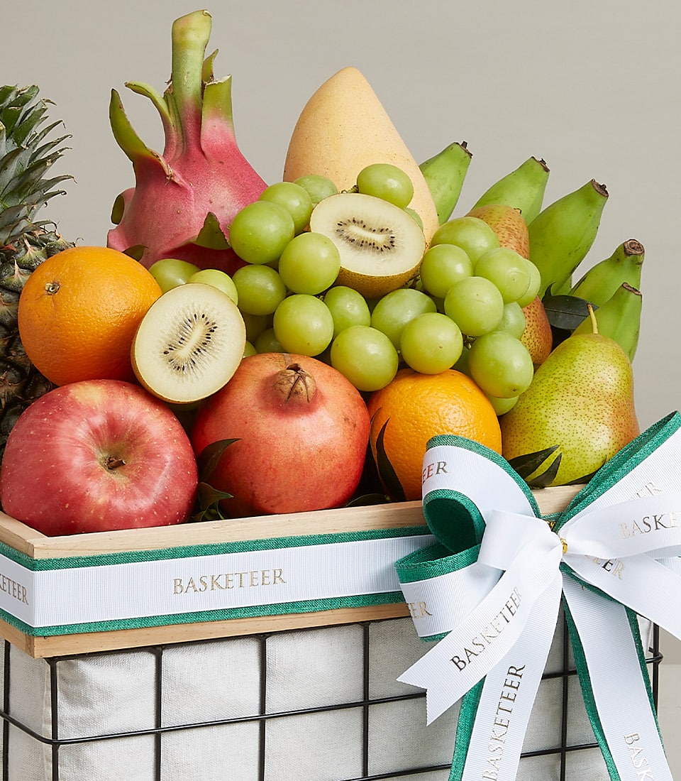 A sumptuous Luxury Fruit Basket elegantly overflowing with an exquisite assortment of nature's finest. The selection includes a majestic pineapple, vibrant dragon fruit, crisp apples, zesty oranges, luscious pears, ripe bananas, succulent green grapes, juicy kiwi, and a regal pomegranate. This opulent display is beautifully adorned with a sophisticated white and teal ribbon featuring the distinguished 