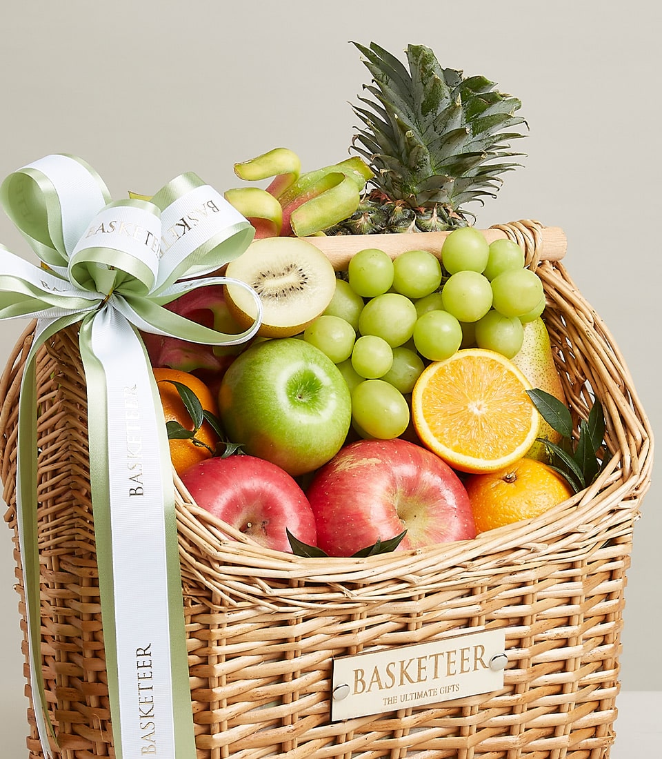 An exquisite fruit hamper, this luxurious wicker basket is elegantly brimming with a selection of the finest fresh fruits—juicy pineapples, succulent grapes, vibrant kiwis, crisp apples, zesty oranges, and sweet bananas. Adorned with an elegant white and green ribbon and featuring a tastefully designed tag that proudly reads 
