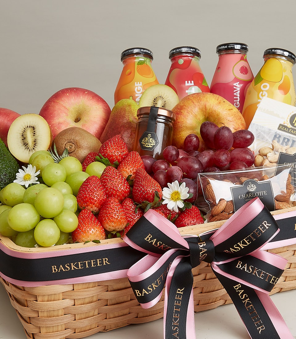 A luxurious wicker basket brimming with a vibrant assortment of fresh fruits like apples, strawberries, grapes, and avocados. The Gourmet Fruit and Nut Gift Basket from Basketeer also features elegantly arranged jars of jam, bottles of juice, and premium packs of nuts. This exquisite presentation is beautifully adorned with a classy pink and black ribbon showcasing the 