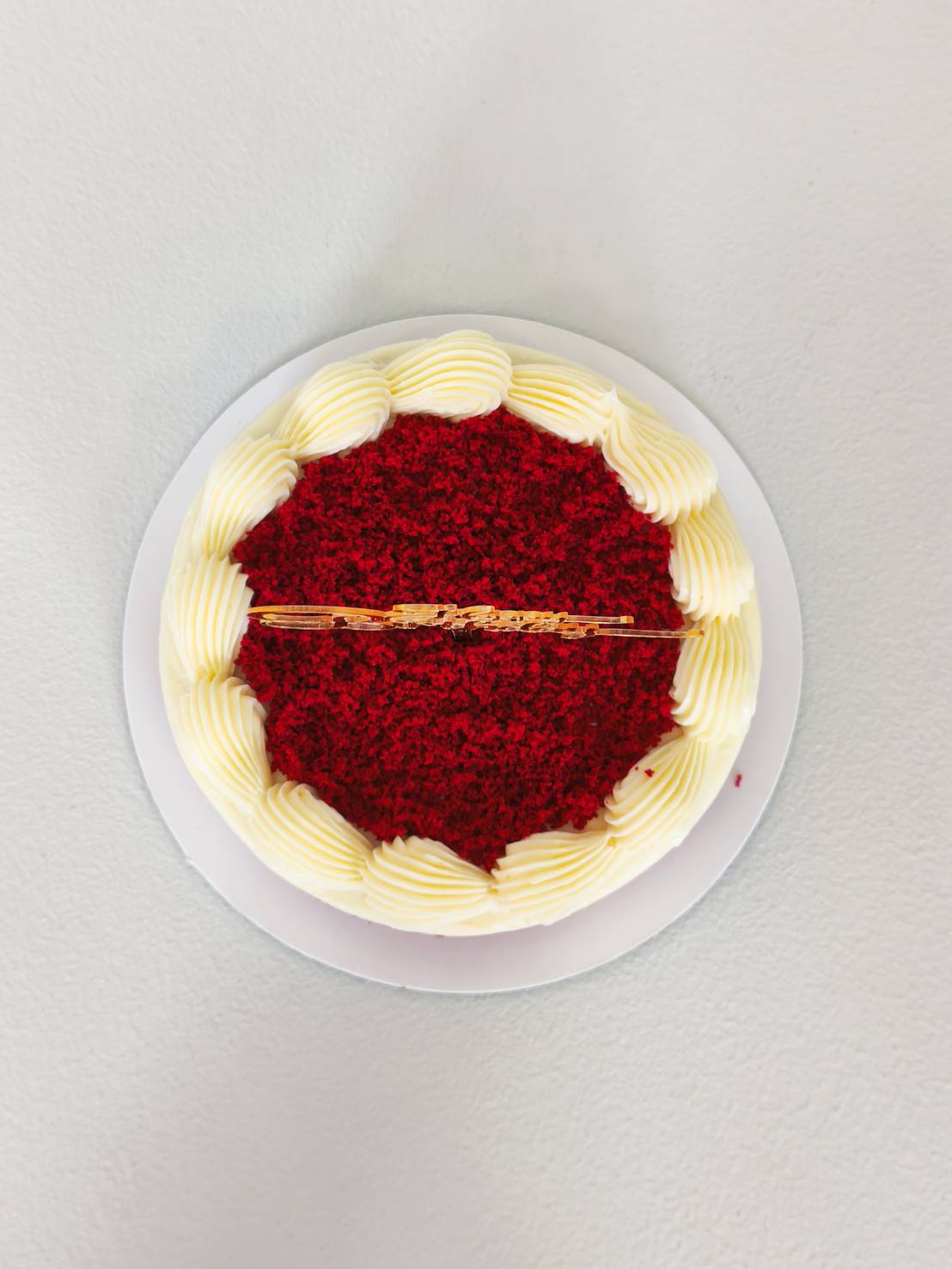 Classic red velvet cake topped with cream cheese frosting and red velvet crumbs, decorated with golden Happy Birthday topper.