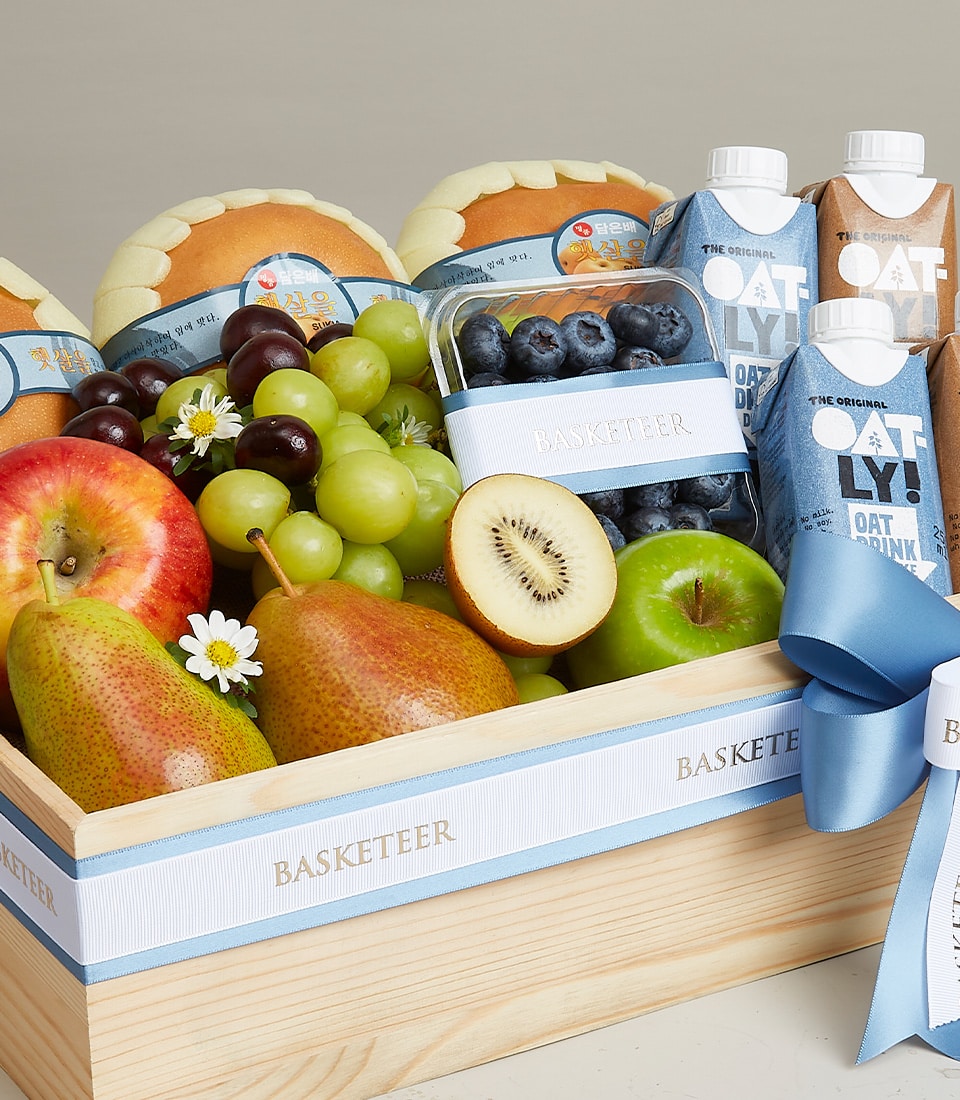 A luxurious wooden basket brimming with an exquisite assortment of fresh fruits and indulgent beverages. Nestled within, discover succulent apples, luscious pears, vibrant grapes, juicy kiwi, and plump blueberries, accompanied by artisanal sweet bread rolls and premium cartons of creamy oat milk. This elegant presentation is adorned with sophisticated blue and white ribbons and proudly features a label reading 