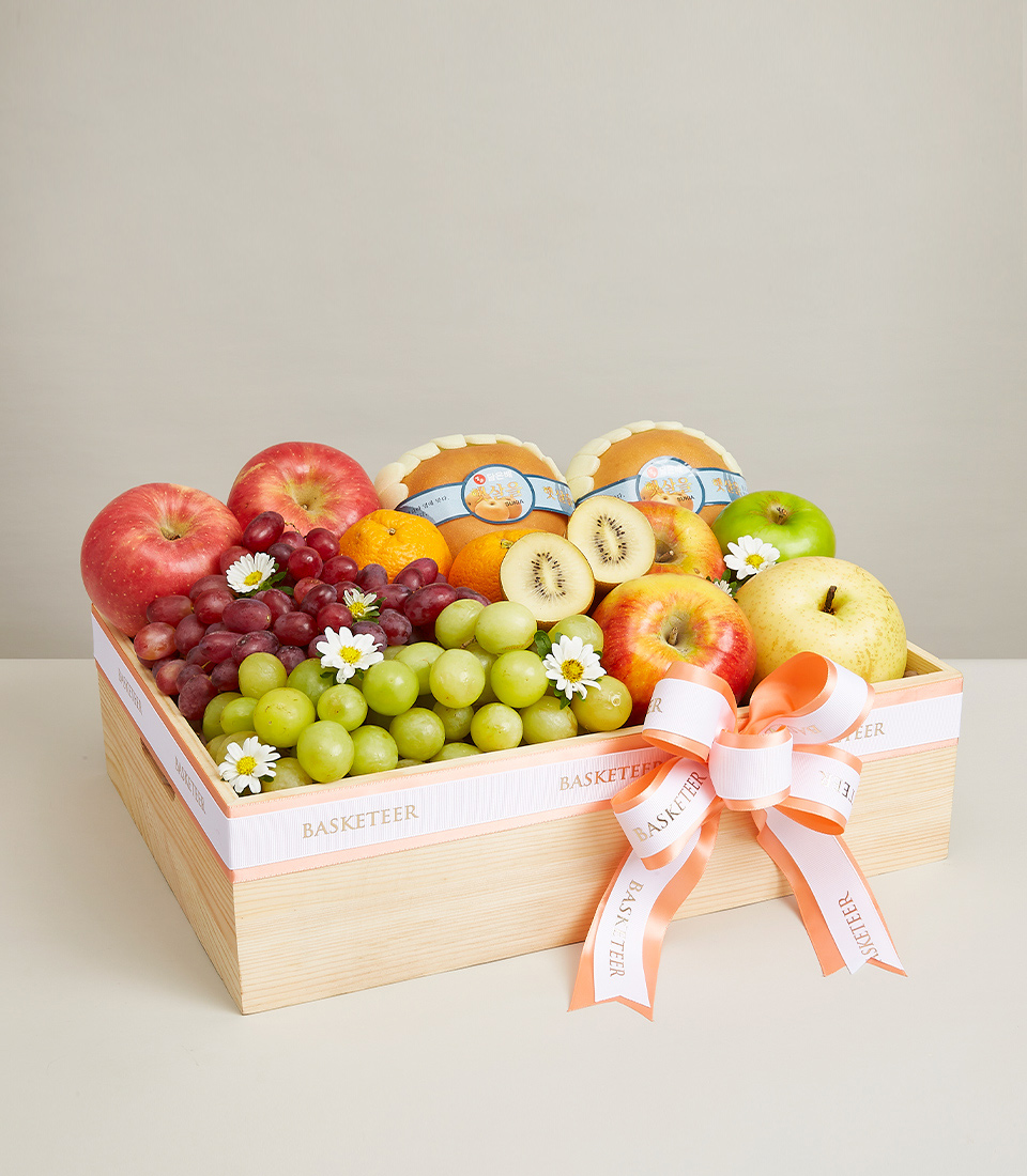 A Gift boxes filled with a variety of fresh fruits such as red grapes, green kiwis, red apples, oranges, and many more. Beautifully decorated with bows, orange and white ribbons with the word “Basketeer” beautifully.