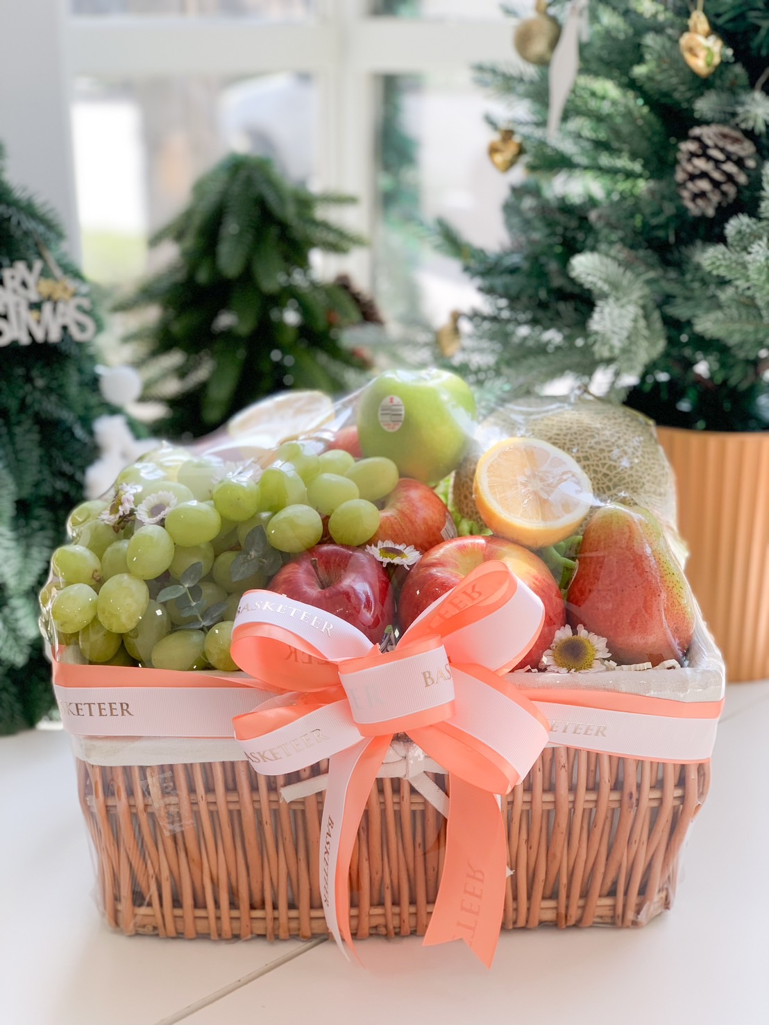 Fresh fruit gift basket with grapes, apples, pears, and cantaloupe, wrapped in a wicker basket and adorned with a peach ribbon.