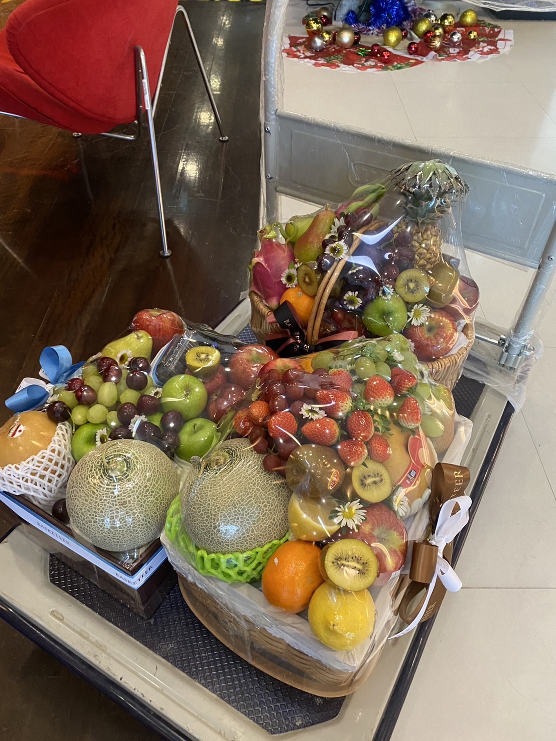 A set of premium fruit baskets filled with strawberries, grapes, melons, kiwi, and dragon fruit, elegantly wrapped and placed on a cart.