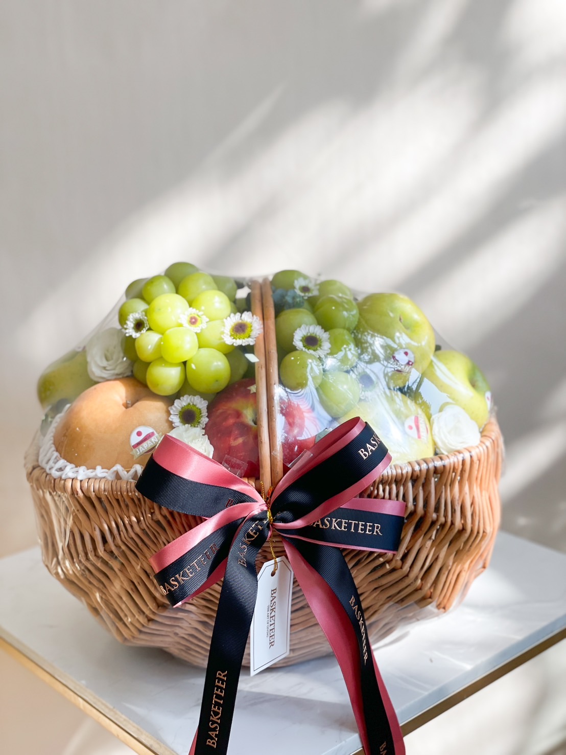 A premium fruit basket filled with Japanese pears, green grapes, apples, and decorated with daisies. Wrapped in a wicker basket with a luxurious ribbon.