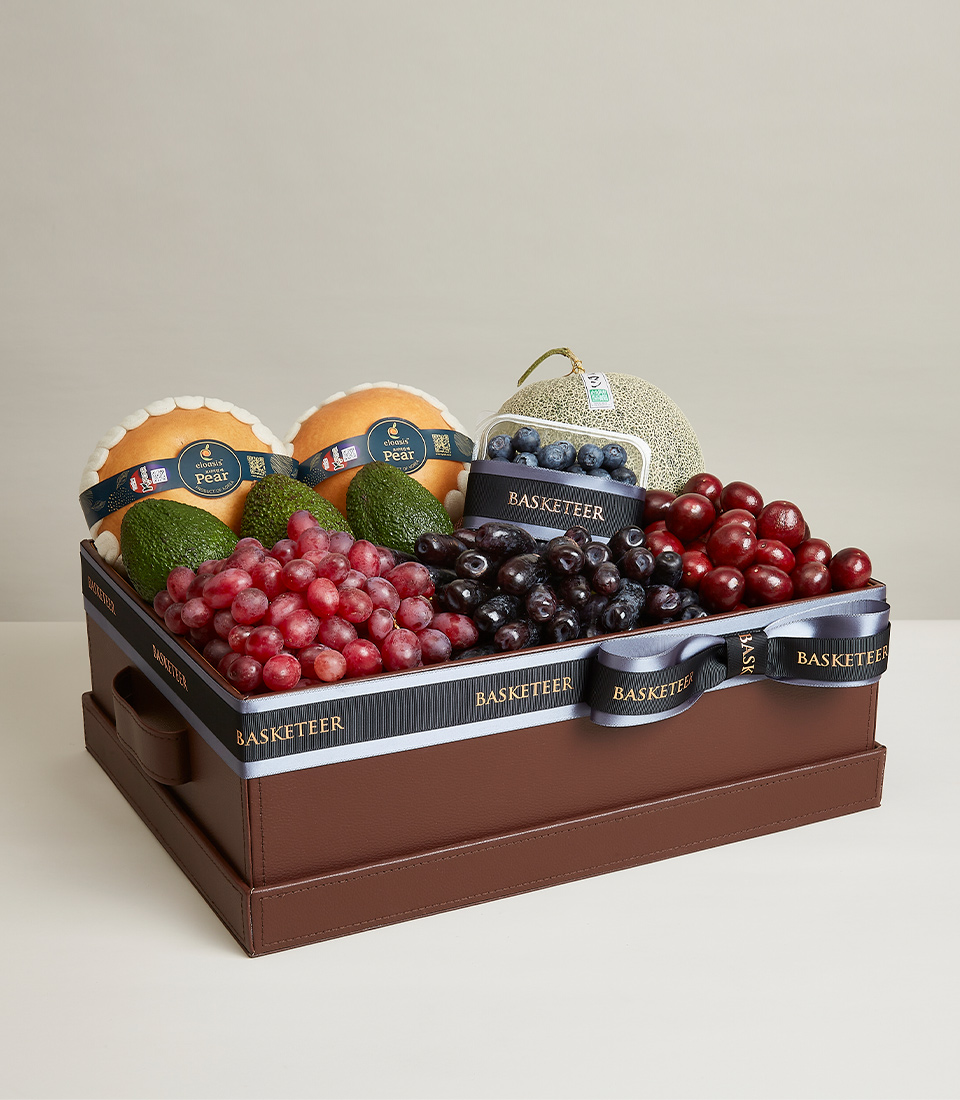 A brown gift box Filled with various kinds of fresh fruits such as green avocados, red grapes, red cherries, and more, it is decorated with light blue and black ribbon bows with 