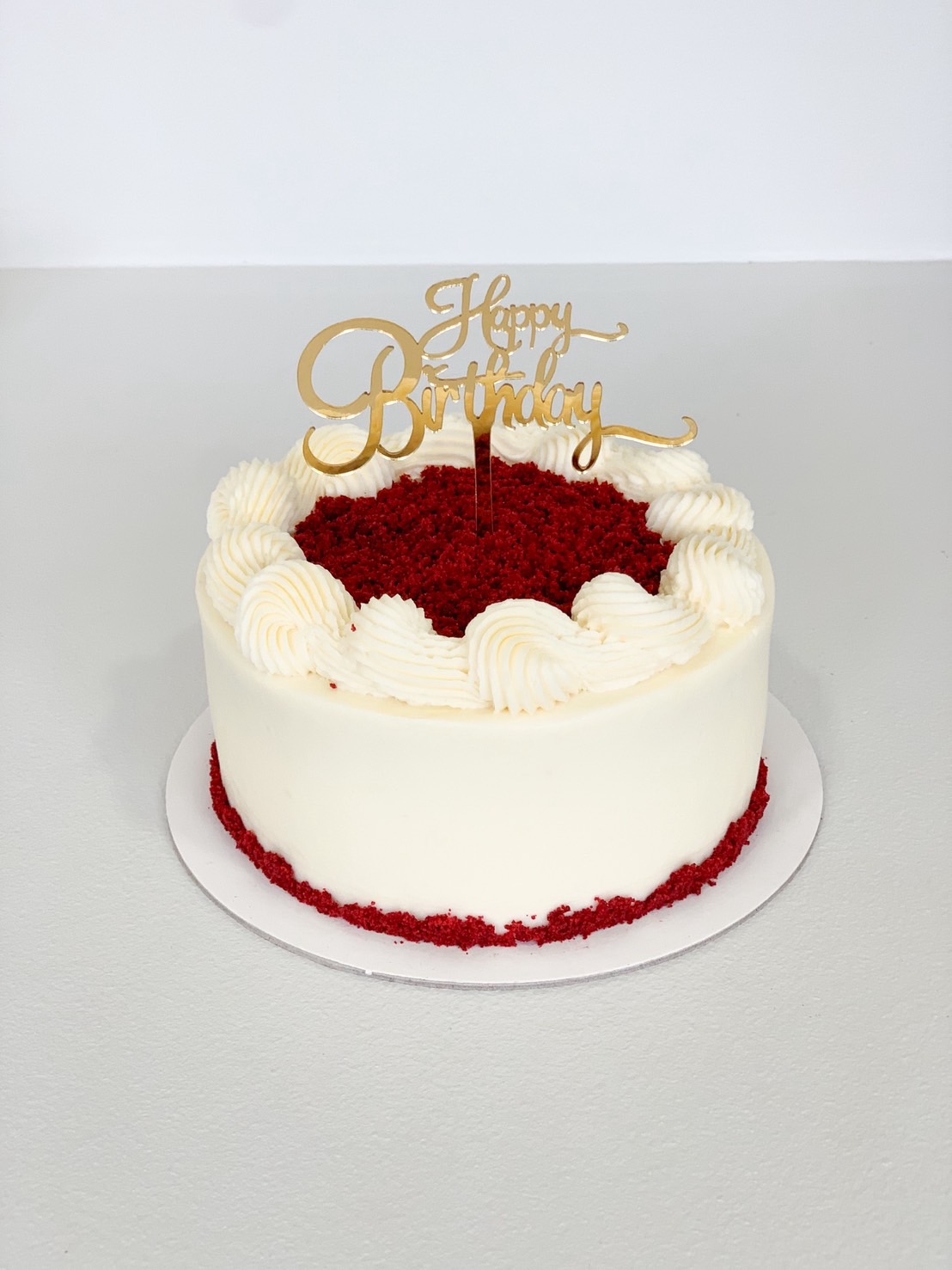Red velvet cake with cream cheese frosting and gold Happy Birthday topper.