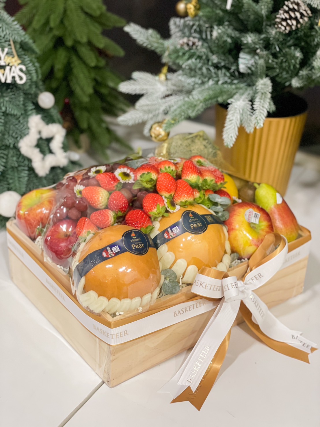 Wooden crate filled with a variety of fresh fruits, including Korean pears, strawberries, apples, and grapes, tied with a white and gold Basketeer ribbon.