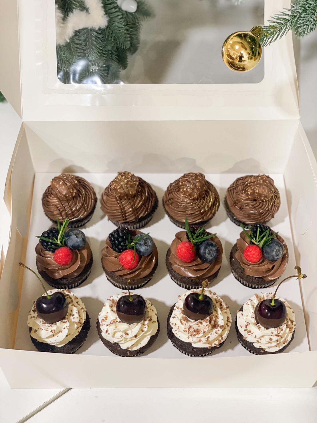 A box of 12 gourmet chocolate cupcakes, topped with chocolate ganache, fresh berries, and whipped cream with cherries.