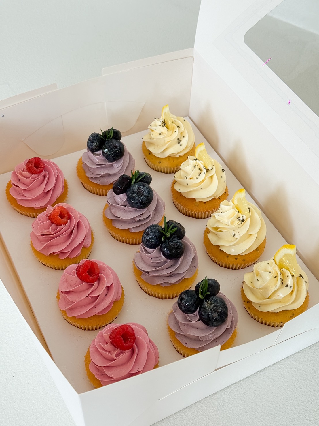 Nine berry cupcakes—raspberry, blueberry, and lemon—nestled in rows in a white box from Charlotte Bakery, Bangkok.