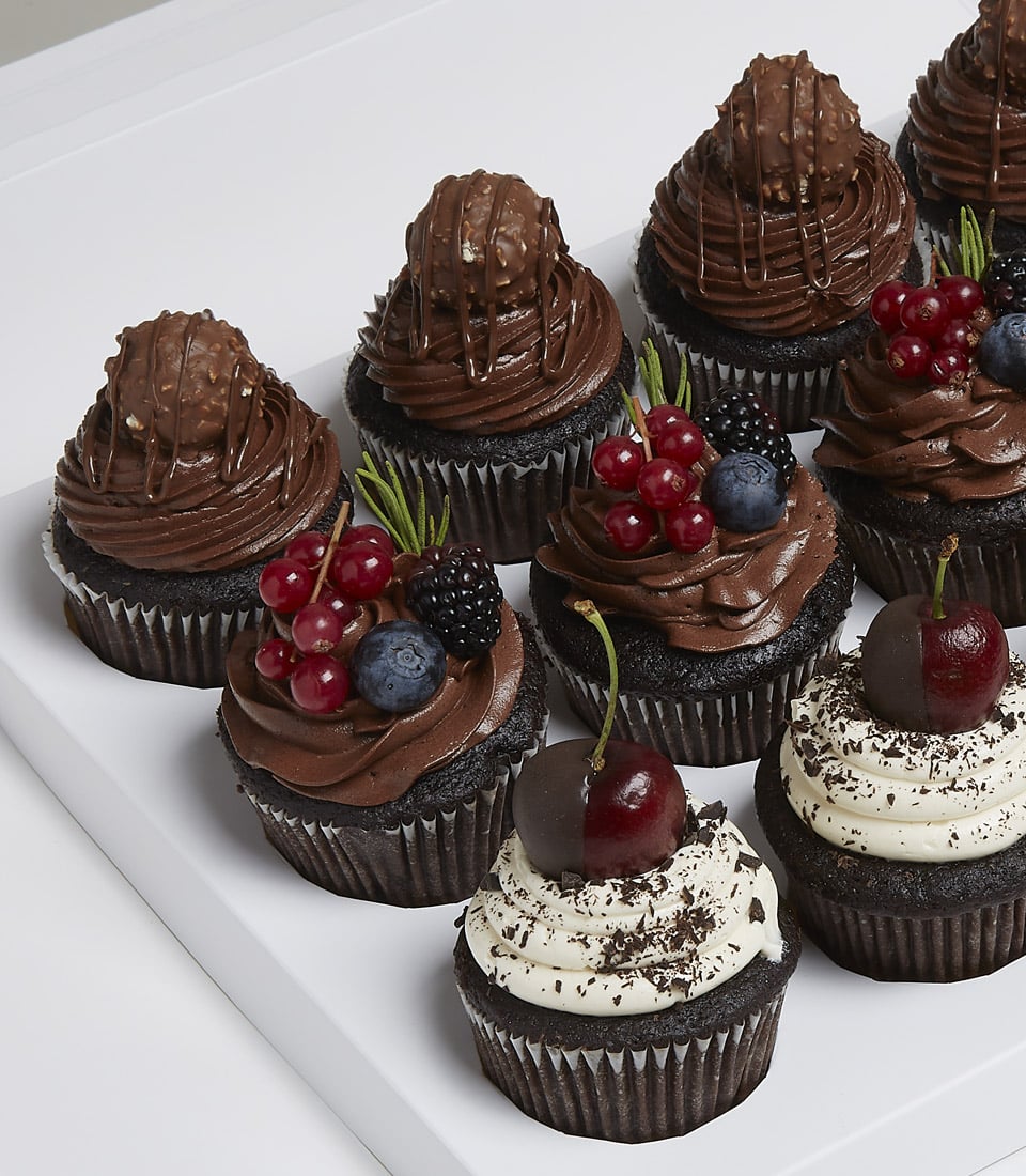 Immerse yourself in the decadent elegance of Basketeer’s gourmet delight: nine meticulously crafted chocolate cupcakes arranged on a pristine white tray. Five sumptuous cupcakes boast rich chocolate frosting crowned with luxurious Ferrero Rocher chocolates, exuding indulgence. Three more are lavishly adorned with silky chocolate frosting and an assortment of fresh, luscious berries, inviting a burst of flavor with every bite. The crowning jewel is a single cupcake graced with velvety white frosting and topped by a perfectly dipped chocolate cherry, promising pure bliss. Presented in an opulent Basketeer box complete with our signature ribbon, this display is the epitome of sweet sophistication and luxury.
