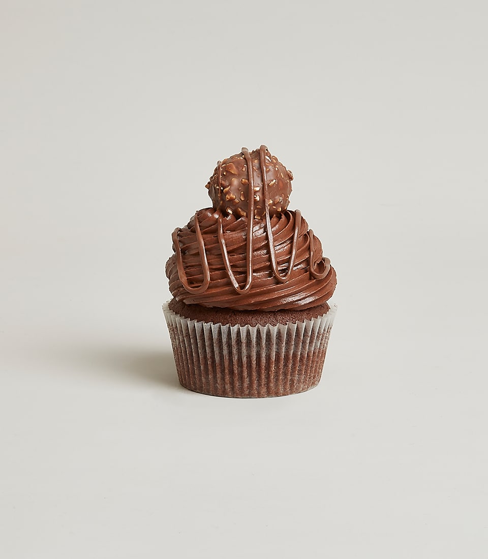 A decadent chocolate cupcake crowned with rich, velvety chocolate frosting and elegantly topped with a luxurious Ferrero Rocher chocolate. The creation is drizzled with luscious streams of additional chocolate, inviting you to indulge in its opulence. The scene harmoniously complements the extravagance of Basketeer’s signature Mix And Match Berry Cupcakes, presented against a pristine white background that elevates the allure of this sumptuous treat.