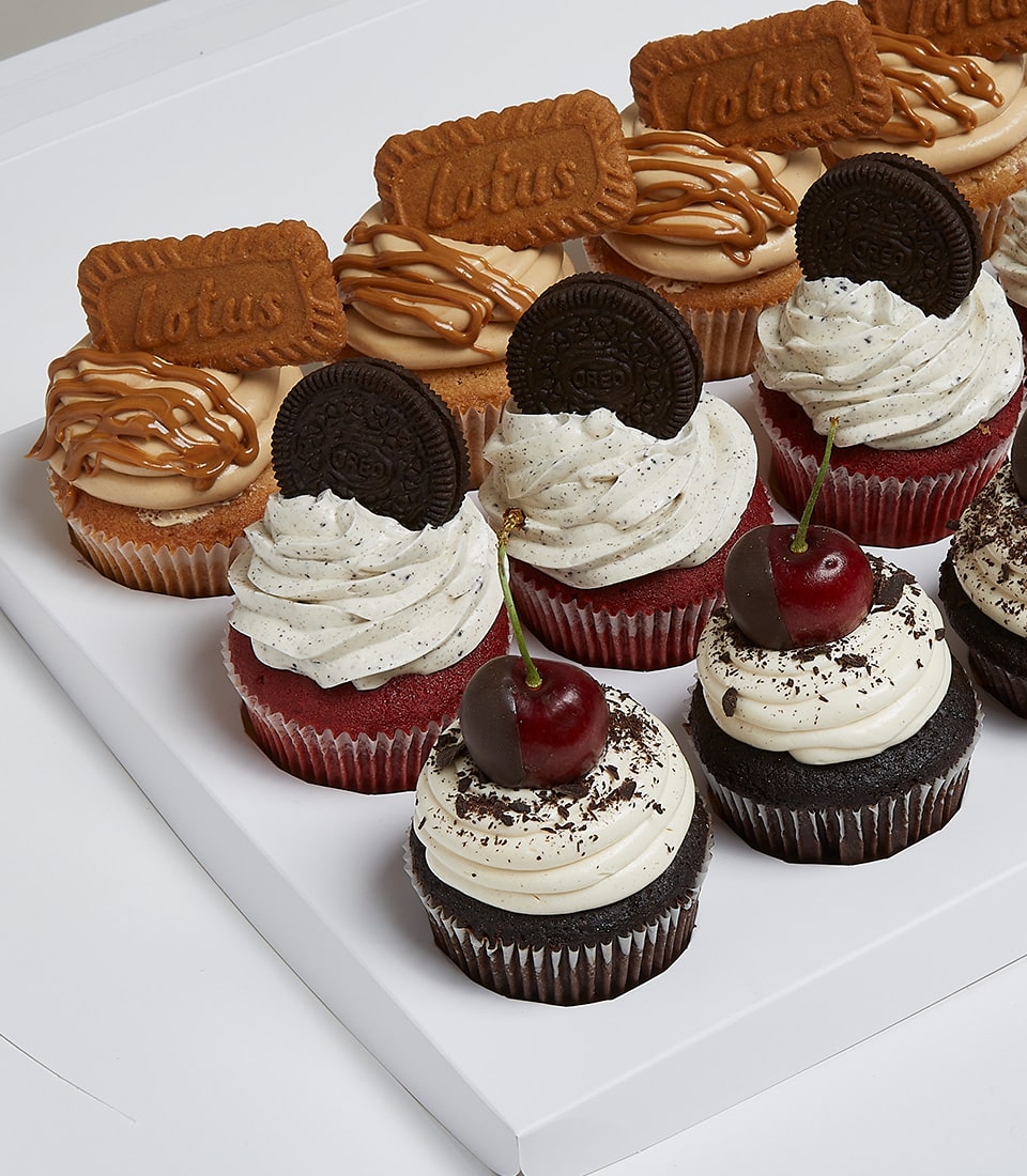 A luxurious Basketeer box filled with an exquisite selection of Mix and Match Cupcakes, artfully arranged in elegant rows. Each variety promises a delightful indulgence: decadent cupcakes adorned with Lotus Biscoff cookies and a caramel drizzle, sumptuous cupcakes featuring Oreo cookies crowned with fluffy whipped cream, and opulent cupcakes topped with plump cherries and delicate chocolate shavings on a cloud of whipped cream. The Basketeer logo graces the ribbon that ties this gourmet assortment together, exuding sophistication and inviting you to savor every bite.