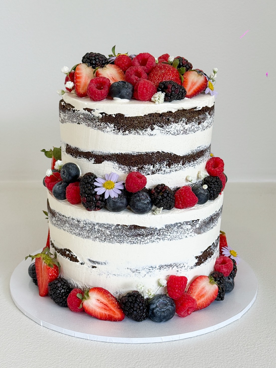 Two-tier chocolate naked cake decorated with strawberries, raspberries, blueberries, blackberries, and small flowers.