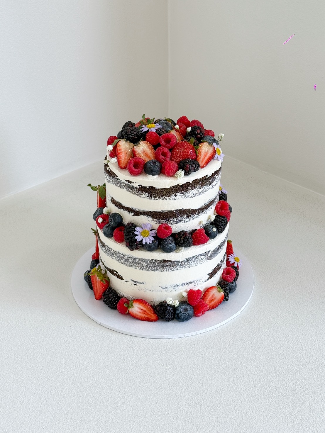 Two-tier naked chocolate cake decorated with strawberries, raspberries, blueberries, blackberries, and small edible flowers.