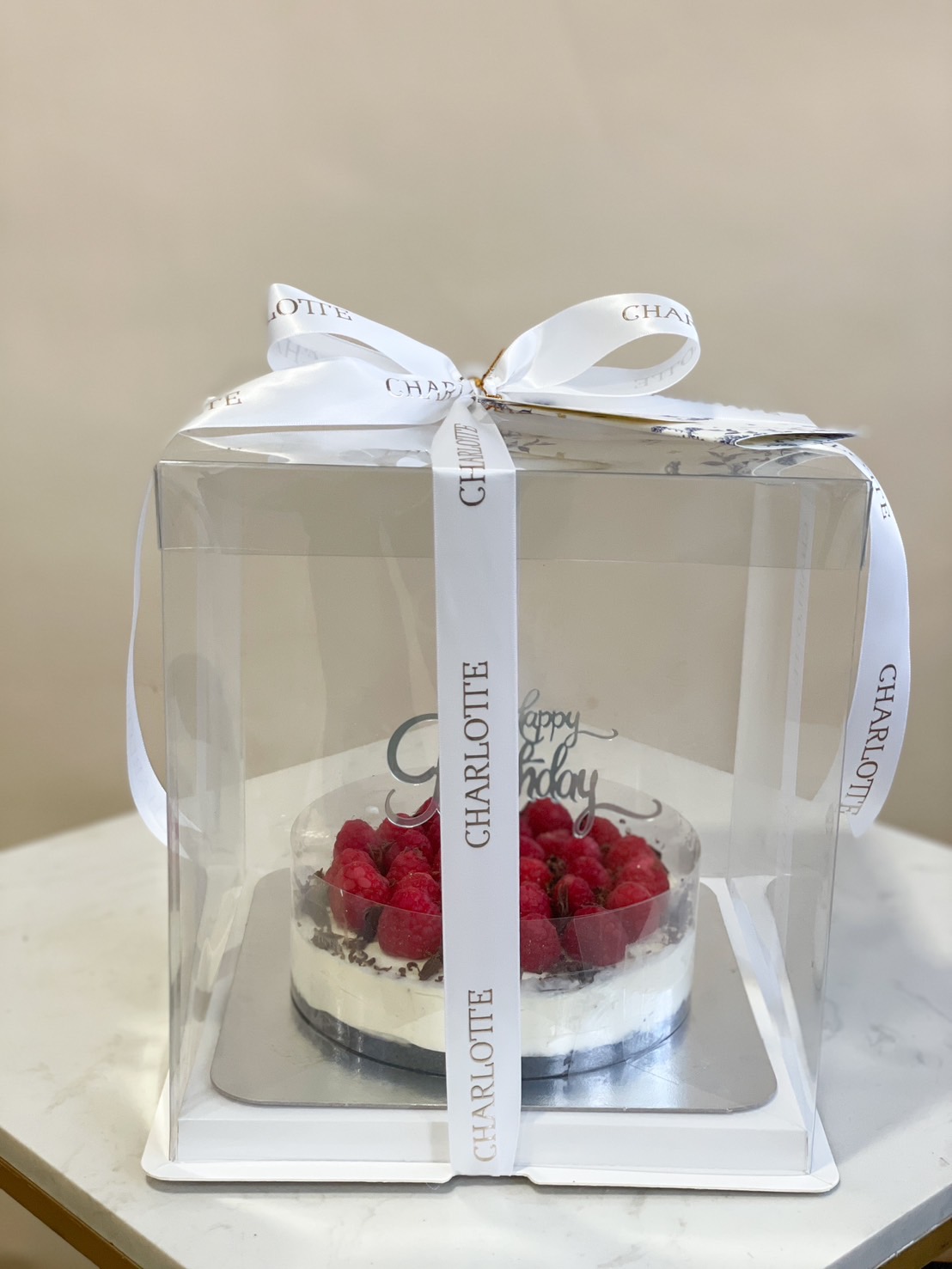 A beautifully wrapped Raspberry Cheesecake, topped with fresh raspberries and chocolate shavings, in an elegant gift box.