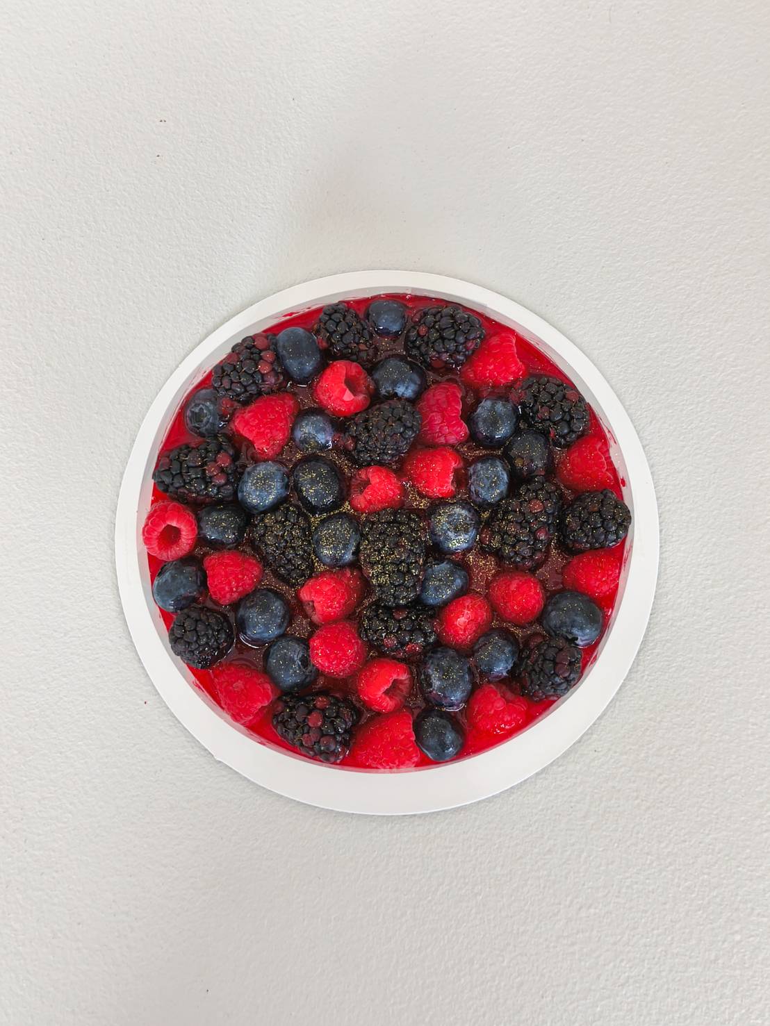 Berry mousse cake topped with fresh raspberries, blueberries, and blackberries glazed with berry jelly.