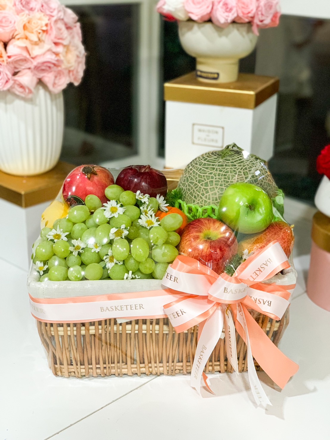 A beautifully arranged luxury fresh fruit basket, featuring grapes, melon, apples, pomegranate, and more, wrapped with a Basketeer ribbon, perfect for gifts and special occasions.