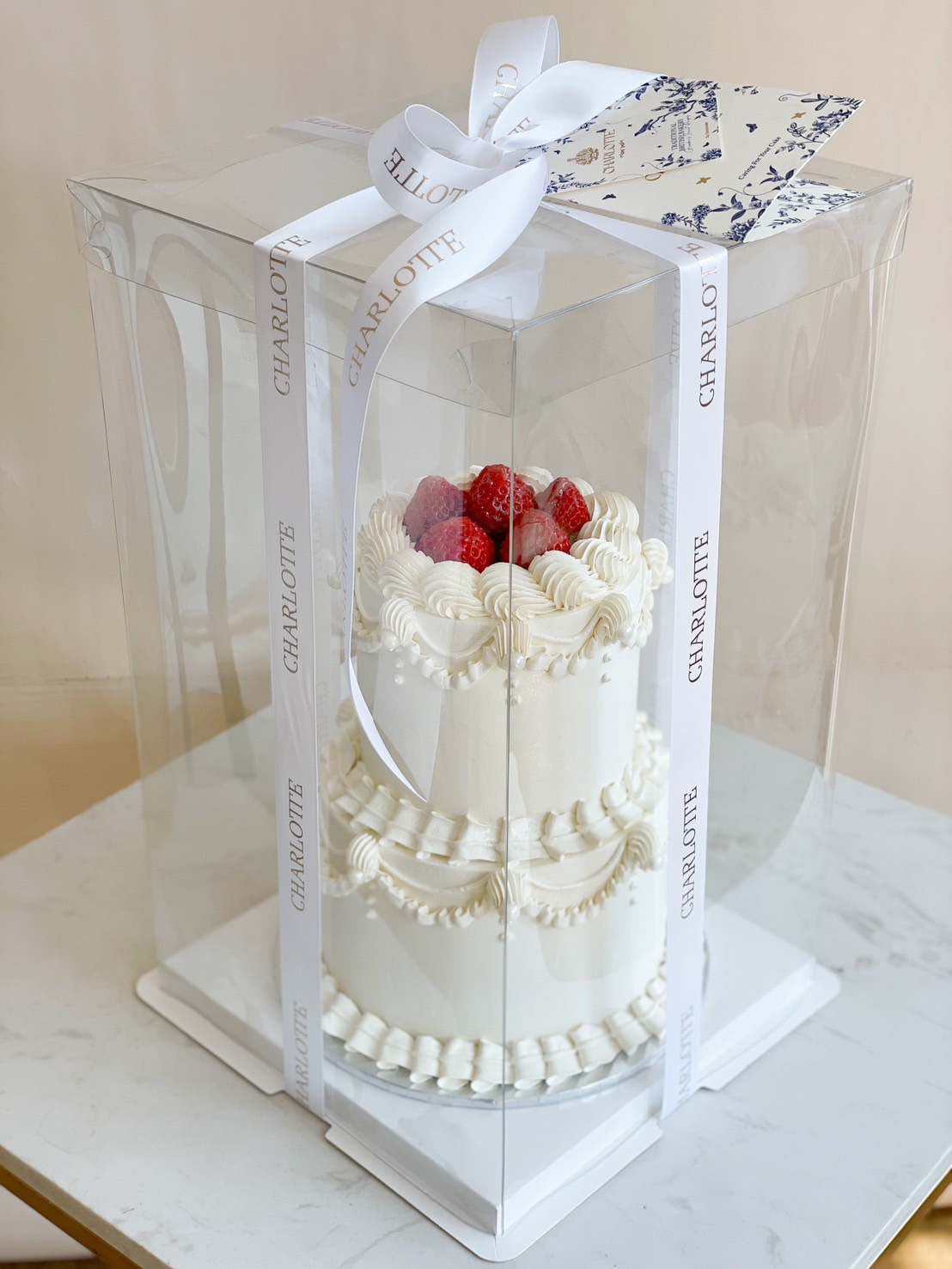 A classic 2-tier white vintage cake, decorated with elegant buttercream piping and fresh strawberries, beautifully packaged in a luxury gift box.