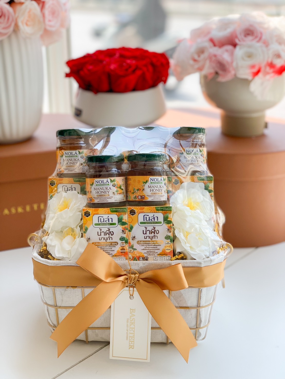 A beautifully arranged Manuka honey gift basket, featuring NOLA Manuka Honey jars and premium honey essence, elegantly wrapped with a soft gold ribbon, floral accents, and a stylish woven basket—perfect for health-conscious gifting, corporate wellness, and special occasions.