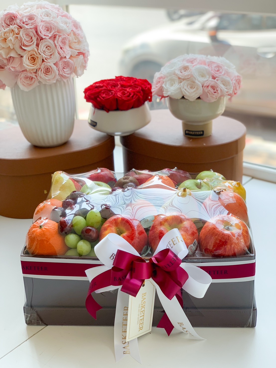 A luxurious fresh fruit gift box filled with premium apples, grapes, oranges, and pears, beautifully wrapped in a sophisticated black box with an elegant red and white ribbon. Perfect for corporate gifting, celebrations, and special occasions.