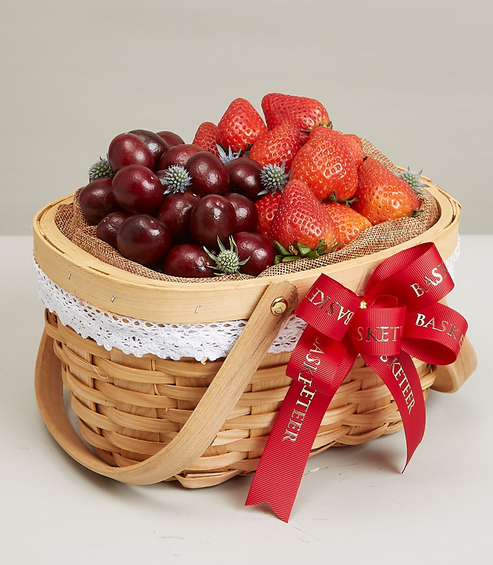 An exquisite wicker basket brimming with a selection of fresh, luscious strawberries and succulent grapes, intertwined with elegant sprigs of verdant leaves. The basket is beautifully adorned with delicate white lace and a luxurious red ribbon proudly showcasing the 