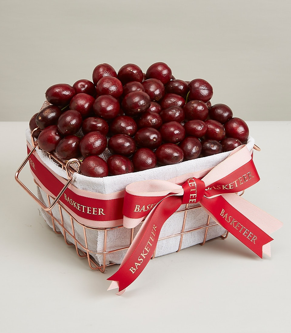 A luxurious wire basket, elegantly lined with pristine white fabric and adorned with rich red ribbons embossed with the iconic 