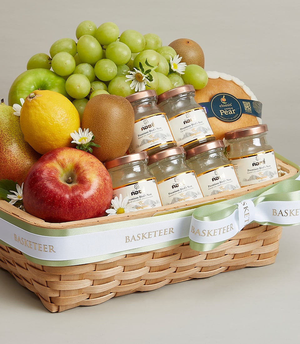A sumptuous wicker basket brimming with an exquisite selection of fresh fruits, including vibrant green grapes, luscious kiwis, a crisp apple, a succulent pear, a zesty lemon, and a sweet melon. Nestled amongst these treasures are elegant jars of delectable pear puree. Adorned with delicate white flowers and an ornate ribbon elegantly emblazoned with the 