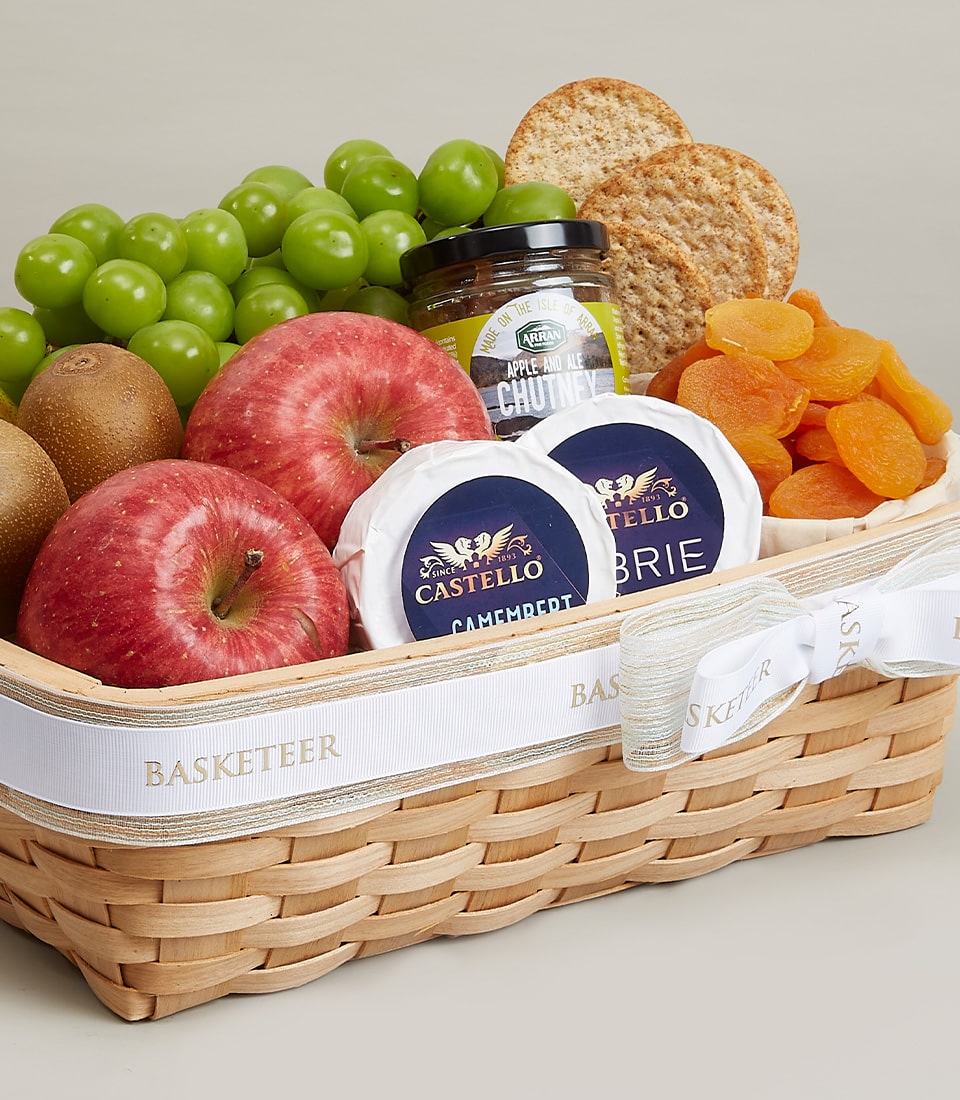 The opulent Fruits & Cheese Harmony Gift Basket from Basketeer boasts an exquisite assortment of succulent green grapes, crisp apples, and vibrant kiwi. Nestled alongside are luscious dried apricots, complemented by two varieties of premium Castello cheese—Camembert and Brie. Delicate water crackers and a jar of gourmet apple and pear chutney complete this luxurious ensemble. The basket exudes elegance with its signature Basketeer ribbon or logo-adorned box, inviting you to indulge in a sophisticated culinary experience.