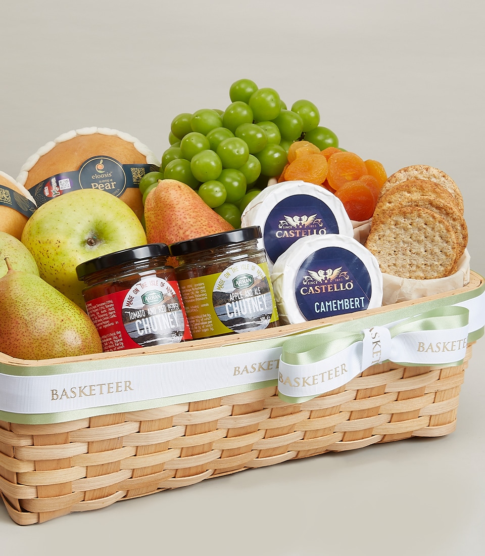 A luxurious wicker gift basket brimming with an assortment of gourmet delights awaits your indulgence. This exquisite arrangement, titled the Cheese & Fresh Harvest Fruits Gift, features plump green grapes, succulent dried apricots, pristine pears, and artisanal round cheese wheels. Accompanied by jars of delectable chutney and crispy bread slices, each item promises a burst of rich flavors. The ensemble is elegantly adorned with a decorative ribbon inscribed with 
