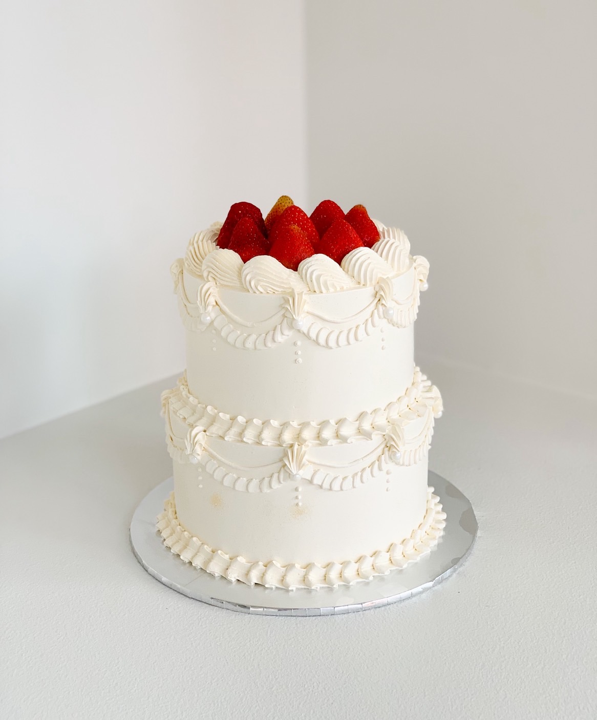 Two-tier vintage white cake with piped cream decorations and fresh strawberries on top