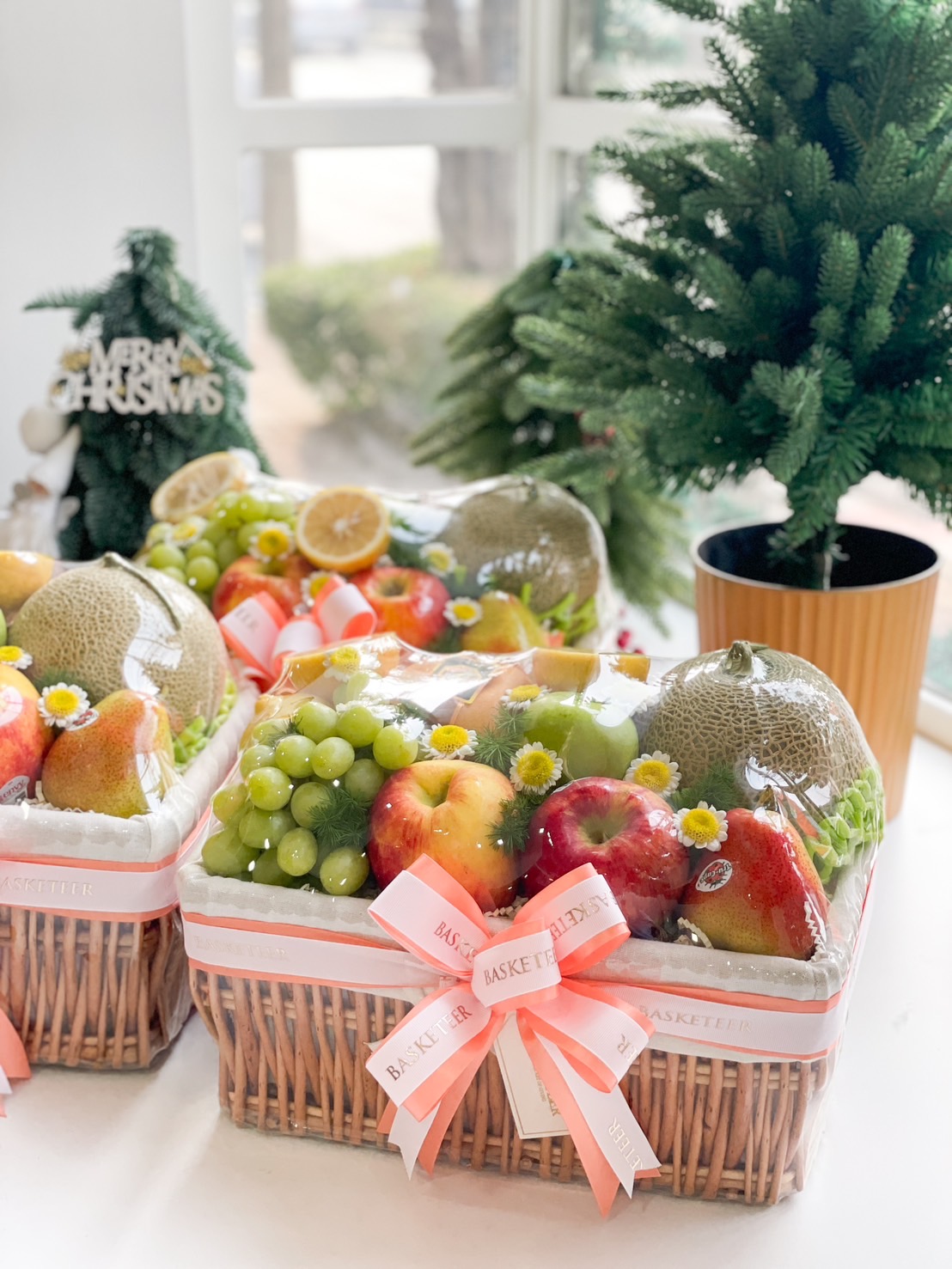 Close up of a Fresh fruit gift basket with grapes, apples, pears, and cantaloupe, wrapped in a wicker basket and adorned with a peach ribbon.